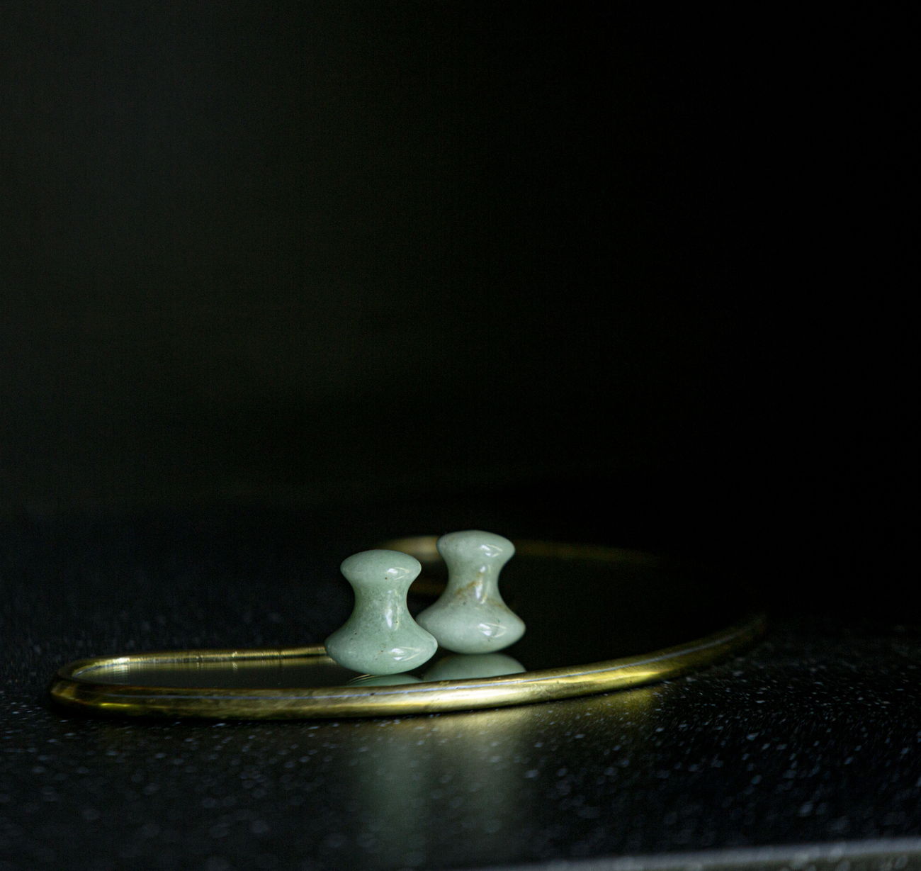 A pair of pale jade Gua Sha mushroom tools resting on a brass tray