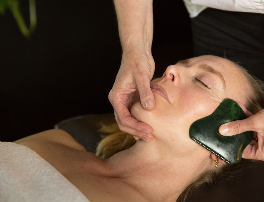 A jade Gua Sha stone drawn along the jawline during a facial treatment