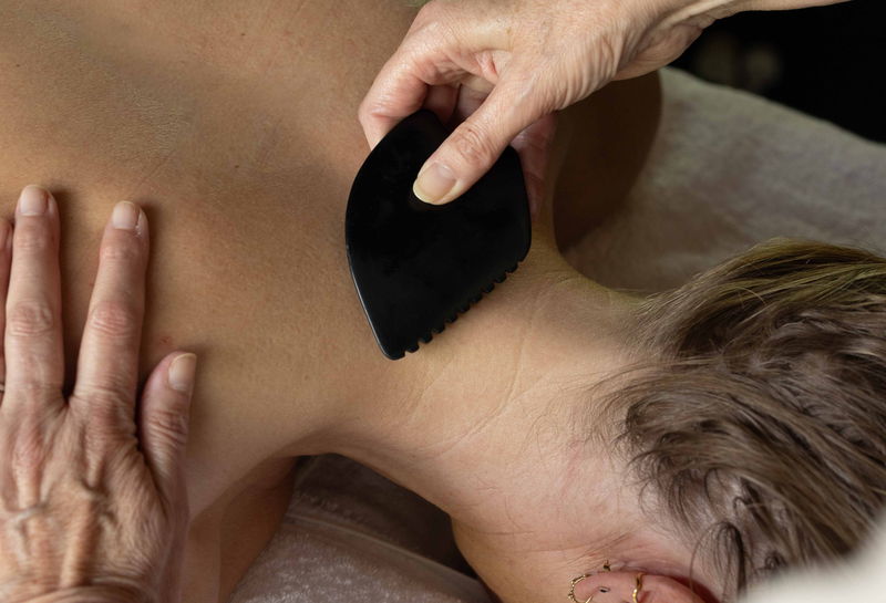 A bian stone Gua Sha tool worked across the shoulder and upper back