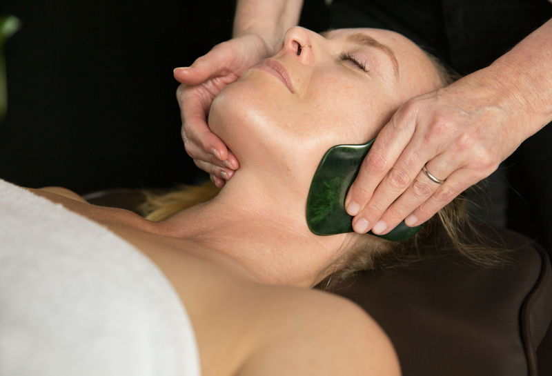 A jade Gua Sha stone sculpting the cheek and jaw